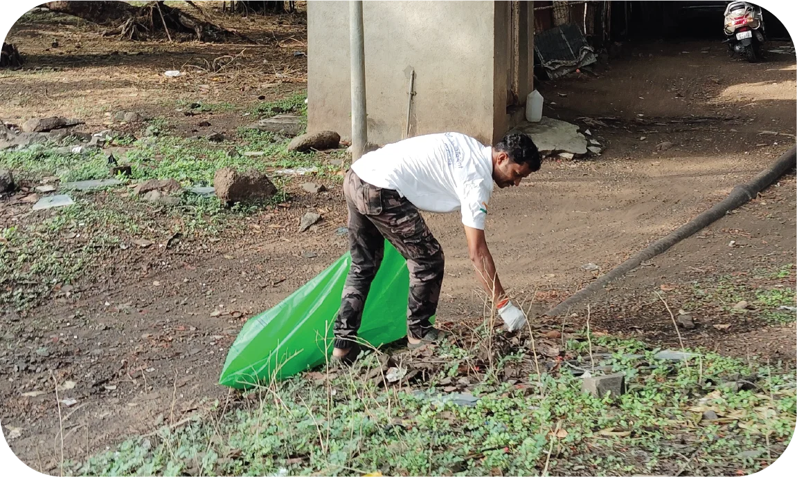 Volunteer picking up litter near a roadside area using a garbage bag